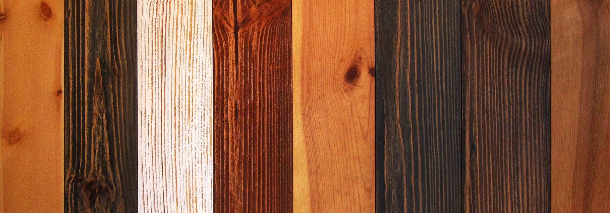 Vertical wooden planks in varying natural, charcoal, and white-washed finishes, softly lit with warm amber and cool blue tones.